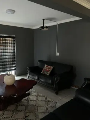 a living room with a black leather couch and a window at Kanyamazane Guesthouse 1214 in eNyamazaneni