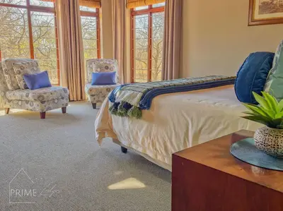 a bedroom with a bed and two chairs and windows at Rhino Lodge at Zebula in Mabula