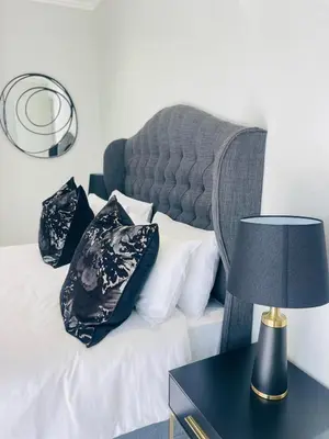 a bed with black and white pillows and a table with a lamp at Apartment Ellipse Waterfall in Midrand