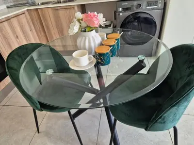 a glass table with two green chairs and a vase with flowers at Tetani's Luxury Oasis in Lakeside