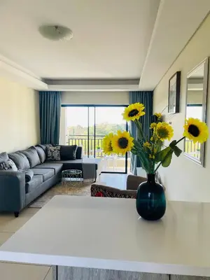 a living room with a vase with yellow flowers on a table at The Classy West End 1 bed with sleeper couch in Midrand