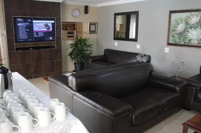 a living room with a leather couch and a television at Firwood Lodge in Pretoria