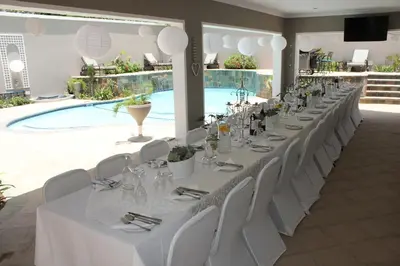 a long table with white chairs and a pool at Firwood Lodge in Pretoria