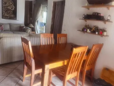 a wooden dining room table with four chairs and a couch at Bosveld Kuier Woonstel in Bela-Bela