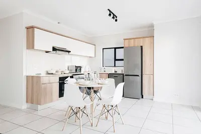 a white kitchen with a table and white chairs at The Blyde Crystal Villa Apartment in Pretoria