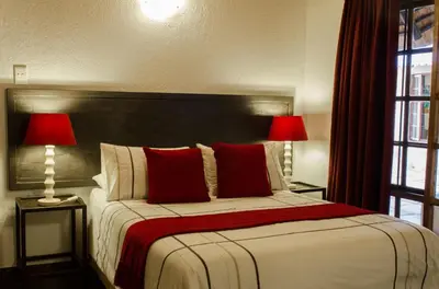 a bedroom with a bed with red pillows and two lamps at Pensão Guest Lodge in Nelspruit