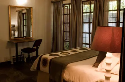 a bedroom with a bed and a desk and windows at Pensão Guest Lodge in Nelspruit
