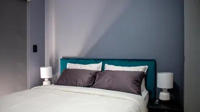a bedroom with a bed with blue walls and two lamps at Time Oon-Travel & Tour Equestria Parkview in Pretoria