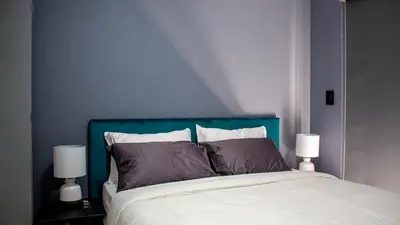 a bedroom with a bed with a blue headboard and two lamps at Time Oon-Travel & Tour Equestria Parkview in Pretoria