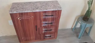 a wooden cabinet with a granite counter top next to a chair at PK house in Mbabat