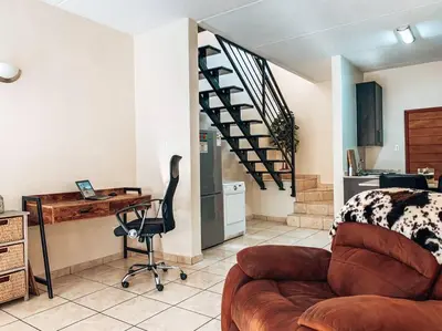 a living room with a couch and a desk and a staircase at Luxury Duplex in Pretoria East in Pretoria