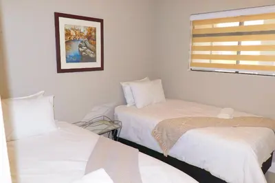 two beds in a room with white sheets and a window at The Thorn by the airport in Kempton Park