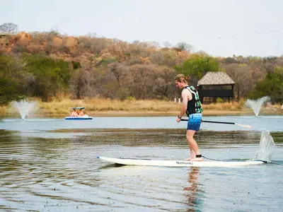 a woman standing on a paddle board in the water at Dikhololo in Brits