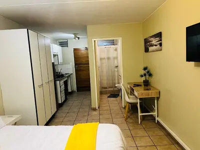 a bedroom with a bed and a desk and a kitchen at Mbizo Cozy Retreat 307 in Pretoria