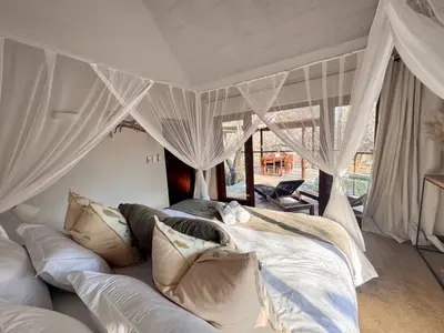 a bedroom with a large bed with white curtains at Raptors Lodge - NXALATI in Hoedspruit