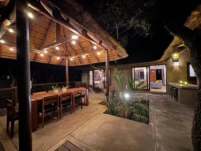 a patio with a table and chairs under a pavilion at night at Raptors Lodge - NXALATI in Hoedspruit