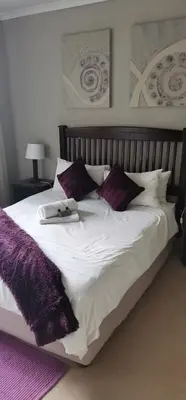 a large white bed with purple pillows on it at Malikana Guesthouse in Kempton Park