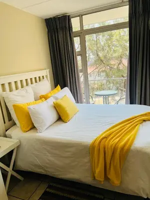 a bed with yellow and white pillows and a window at Mbizo Cozy Retreat 409 in Pretoria