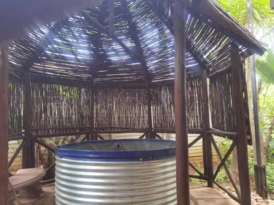 a large metal barrel in a bamboo gazebo at Wooden Log House in Bela-Bela