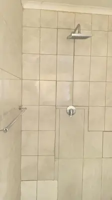 a shower with a white tiled wall at Giraffe camel in Phalaborwa