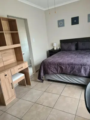 a bedroom with a bed and a wooden desk at Airport Lodge OR Tambo in Kempton Park