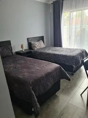a bedroom with two beds and a window and a chair at Airport Lodge OR Tambo in Kempton Park
