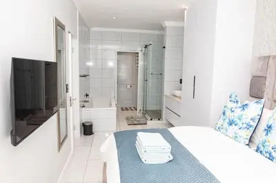 a white bathroom with a bed and a shower at Waterkloof on Main Sassy Modern Apartment in Pretoria
