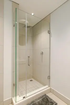 a glass shower in a bathroom with a rug at Neria at Ellipse Waterfall in Midrand