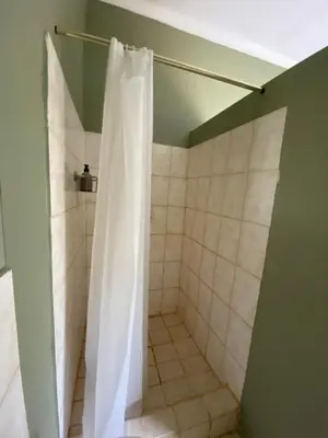 a shower with a white shower curtain in a bathroom at Wildevy Accommodation in Thabazimbi