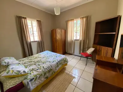 a bedroom with a bed and a desk and windows at Wildevy Accommodation in Thabazimbi