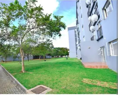 a green yard next to a building with a tree at The Menlyn Hideaway in Pretoria