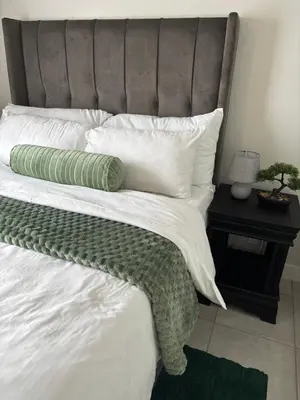 a large bed with white sheets and green pillows at Cozy nest apartment in Pretoria