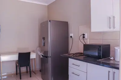 a kitchen with a refrigerator and a table with a chair at Okuhlekwethu Guesthouse in Witbank