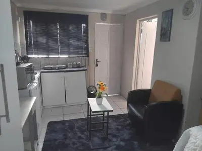 a living room with a table and a chair and a kitchen at Angel Secure Unit in Pretoria