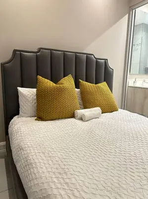 a large bed with yellow pillows and a black headboard at Menlyn Maine Golden Sands in Pretoria