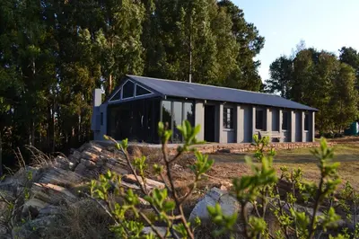a black and white building with trees in the background at Meadow Mist - Self Catering Unit in Dullstroom