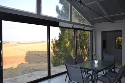 a dining room with a table and chairs and large windows at Meadow Mist - Self Catering Unit in Dullstroom