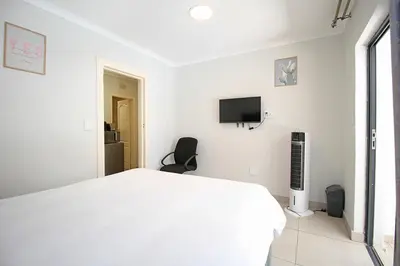 a white bedroom with a bed and a tv at Limewood in Sandton