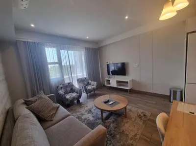 a living room with a couch and chairs and a tv at Lovely 1 Bedroom Apartment in Pretoria
