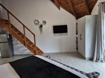 a bedroom with a bed and a staircase with a television at Edel's Nest Nelspruit in Mataffin