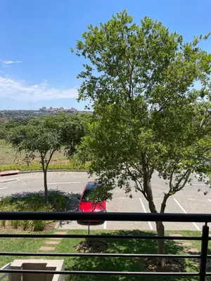 a red car parked in a parking lot with a tree at Tranquil 2 bed 2 bath studio in Sandton