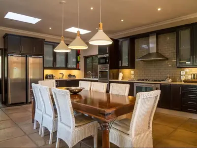 a kitchen with a wooden table and white chairs at African Dream Villa in White River