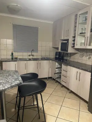 a kitchen with white cabinets and black chairs and a counter at Tan 46 Park Acres in Nelspruit