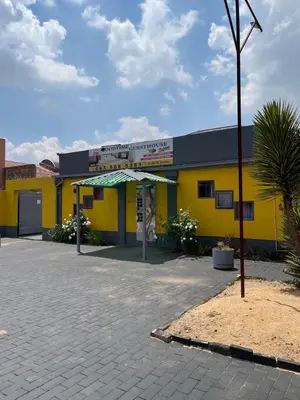 a yellow and black building with a palm tree in front at Good Time Guest House in Springs