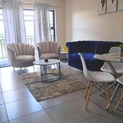 a living room with a blue couch and chairs and a table at Waterfall Ridge Professional Apartment in Midrand