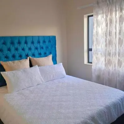 a bed with a blue headboard and a window at Waterfall Ridge Professional Apartment in Midrand