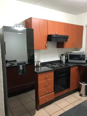 a kitchen with wooden cabinets and a black refrigerator at Cosy duplex in the heart of Midrand in Midrand