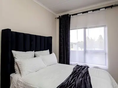 a bedroom with a bed with a black headboard and a window at Urban Retreat in Midrand