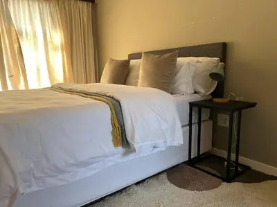 a bedroom with a white bed with a side table at Homie my home in Centurion