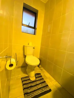 a yellow bathroom with a toilet and a window at Kwena Guesthouse in Groblersdal
